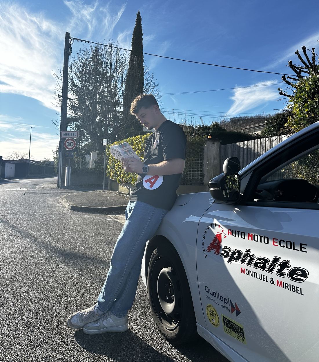 Corentin, enseignant Asphalte, adossé à une voiture-école à l'entrée de Miribel